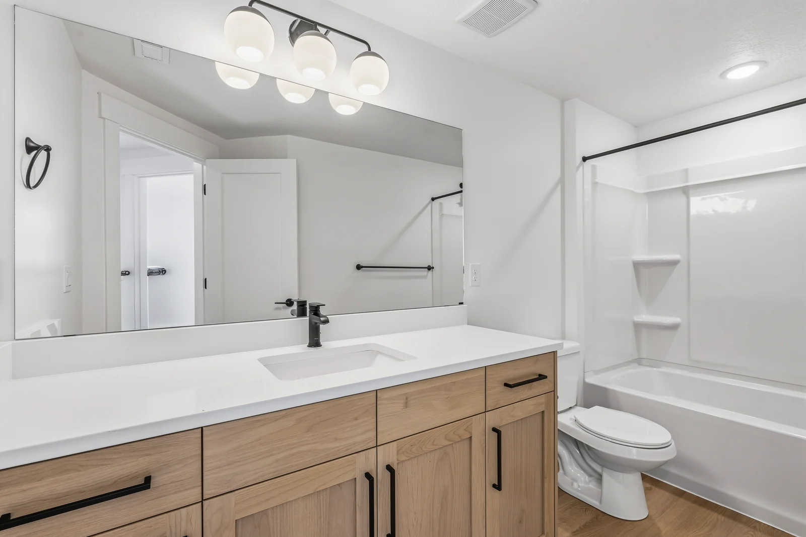 Lower-level bathroom with wood vanity, dark fixtures, toilet, tub-shower surround, and wide mirror at Chestnut MW311, Stansbury Park.
