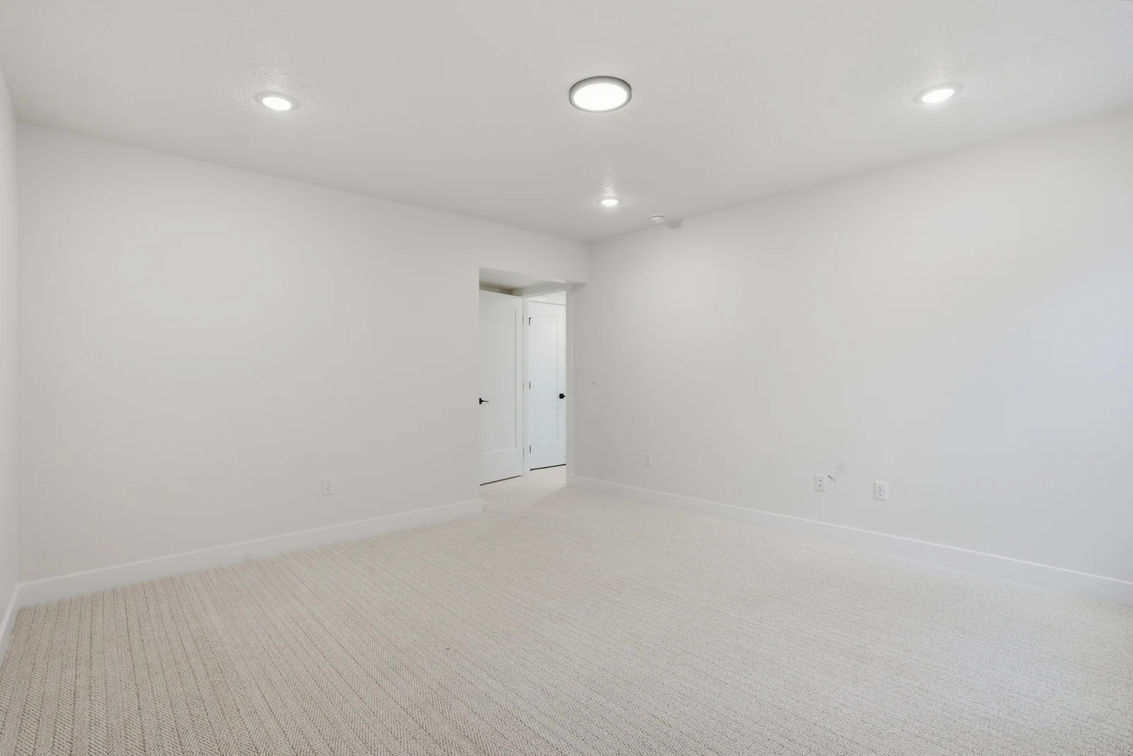 Unfurnished lower-level room with recessed lights, pale carpet, a wide open floor area, and a doorway beyond in the Denali model, American Fork.