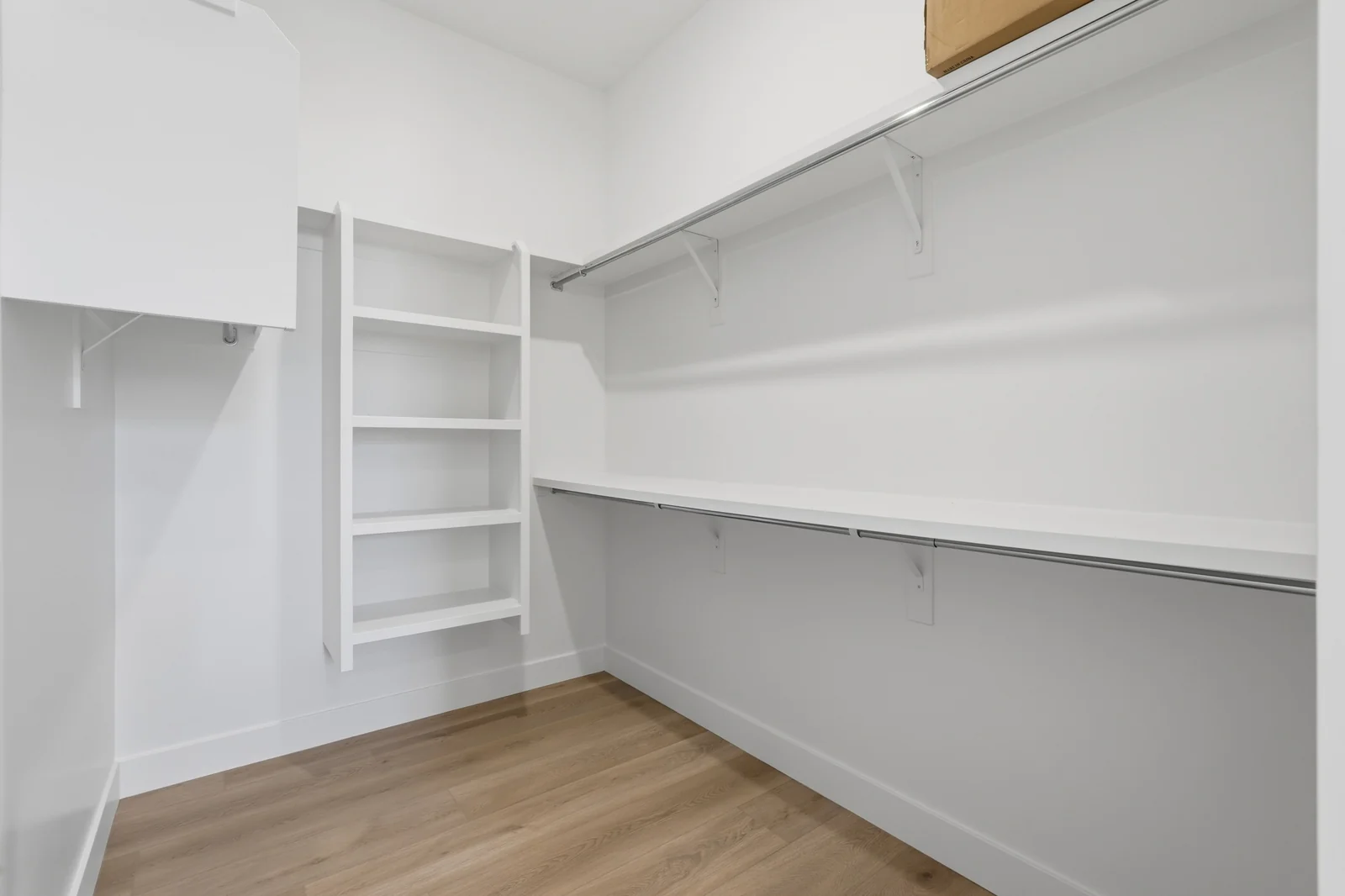 Walk-in closet with wraparound hanging rods, open shelving, and light wood flooring in Chestnut Modern MW302, Stansbury Park.