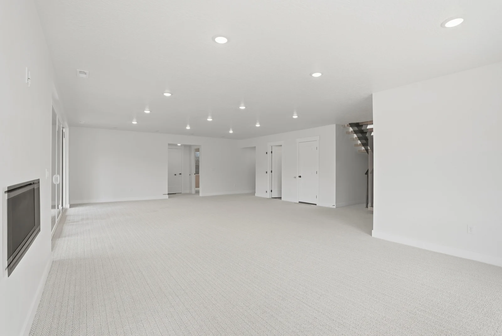 Spacious unfurnished lower-level room with pale carpeting, recessed lighting, a linear fireplace, and multiple doorways in the Denali model, American Fork.