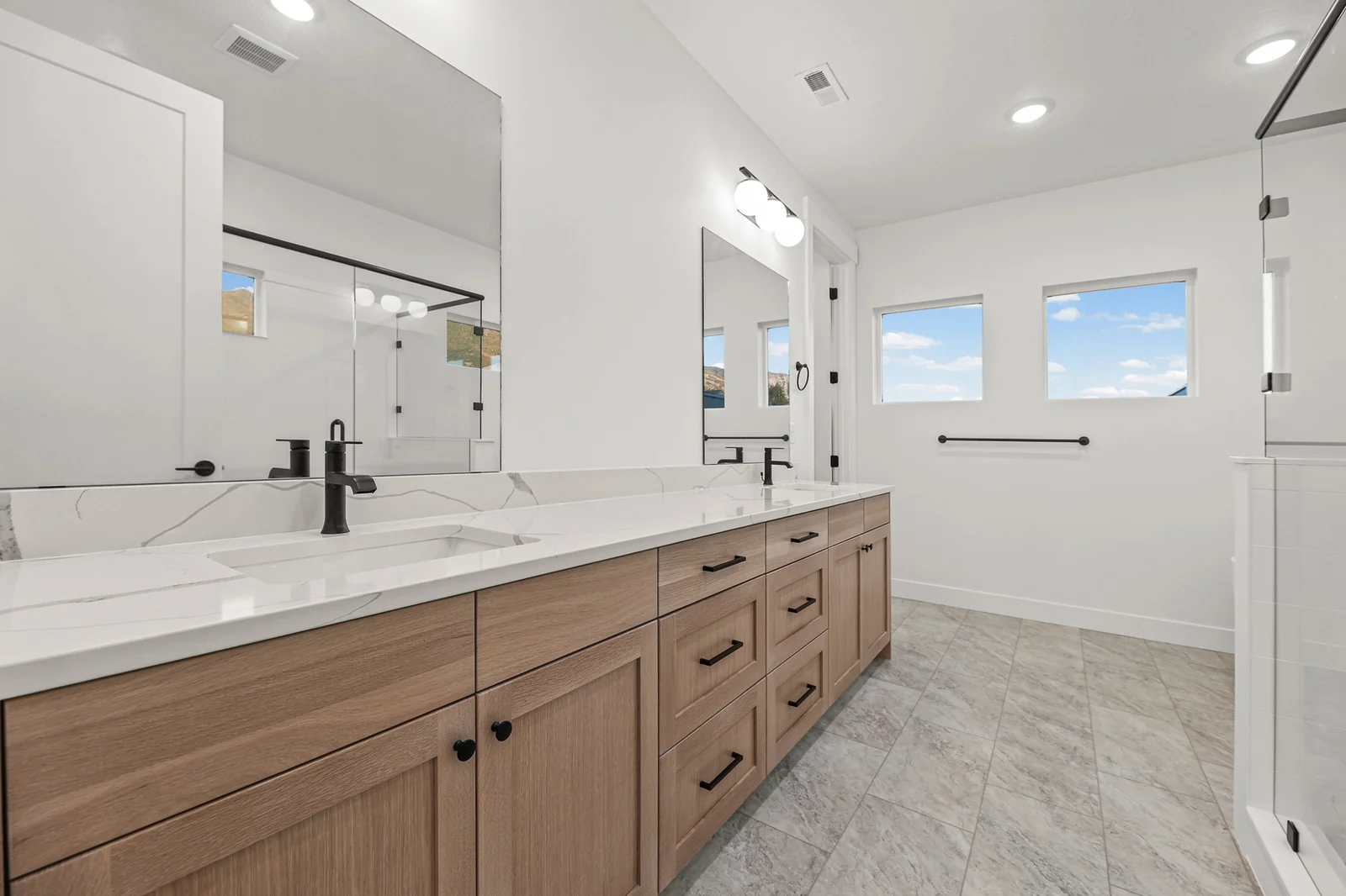 Bathroom with long wood double vanity, large mirror, black fixtures, tile floor, and window in Hawthorne Modern, Ogden.