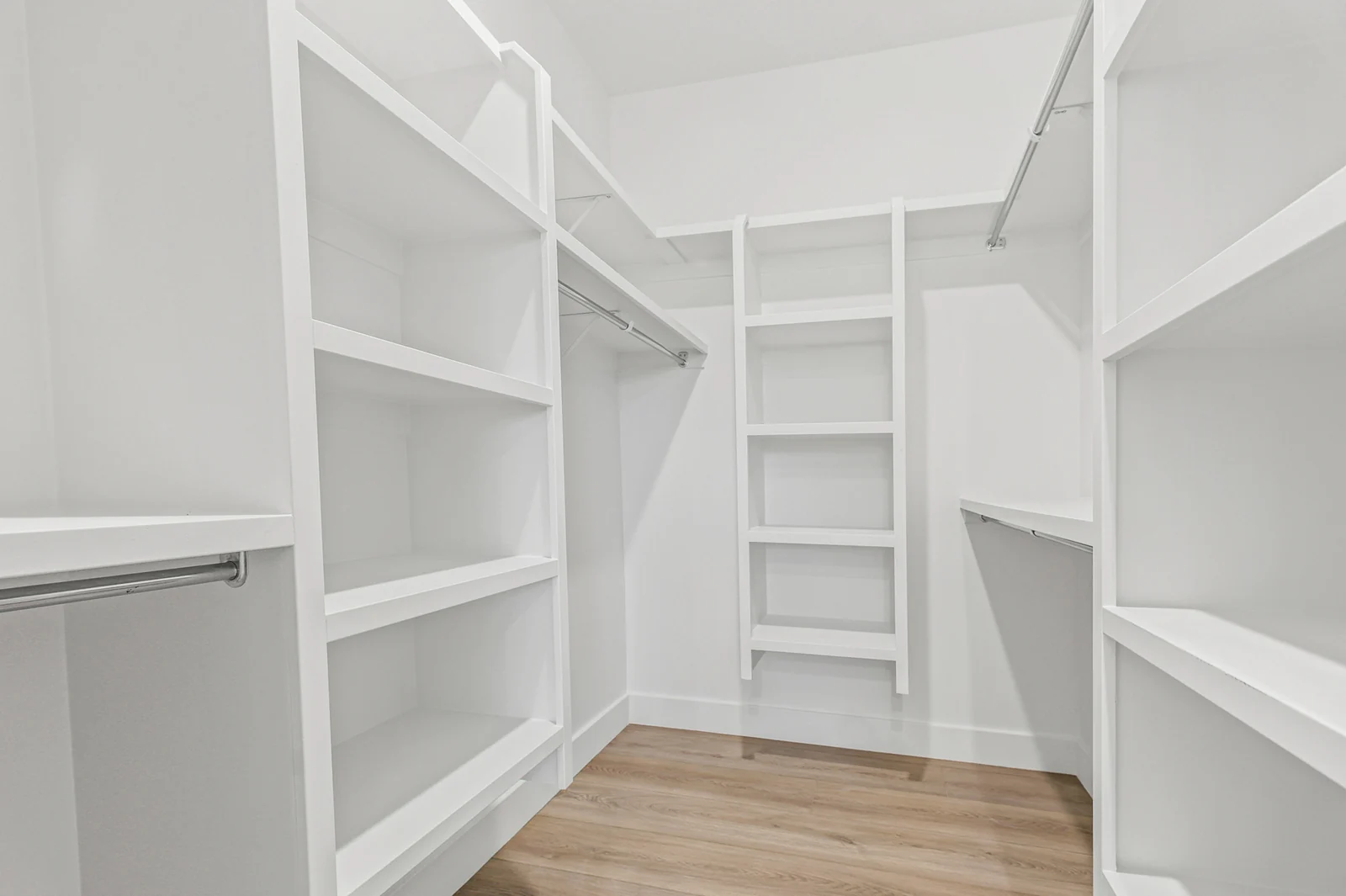 Walk-in closet offers white built-in shelves, hanging rods, storage cubbies, and light wood flooring in Hawthorne Farmhouse, Ogden.