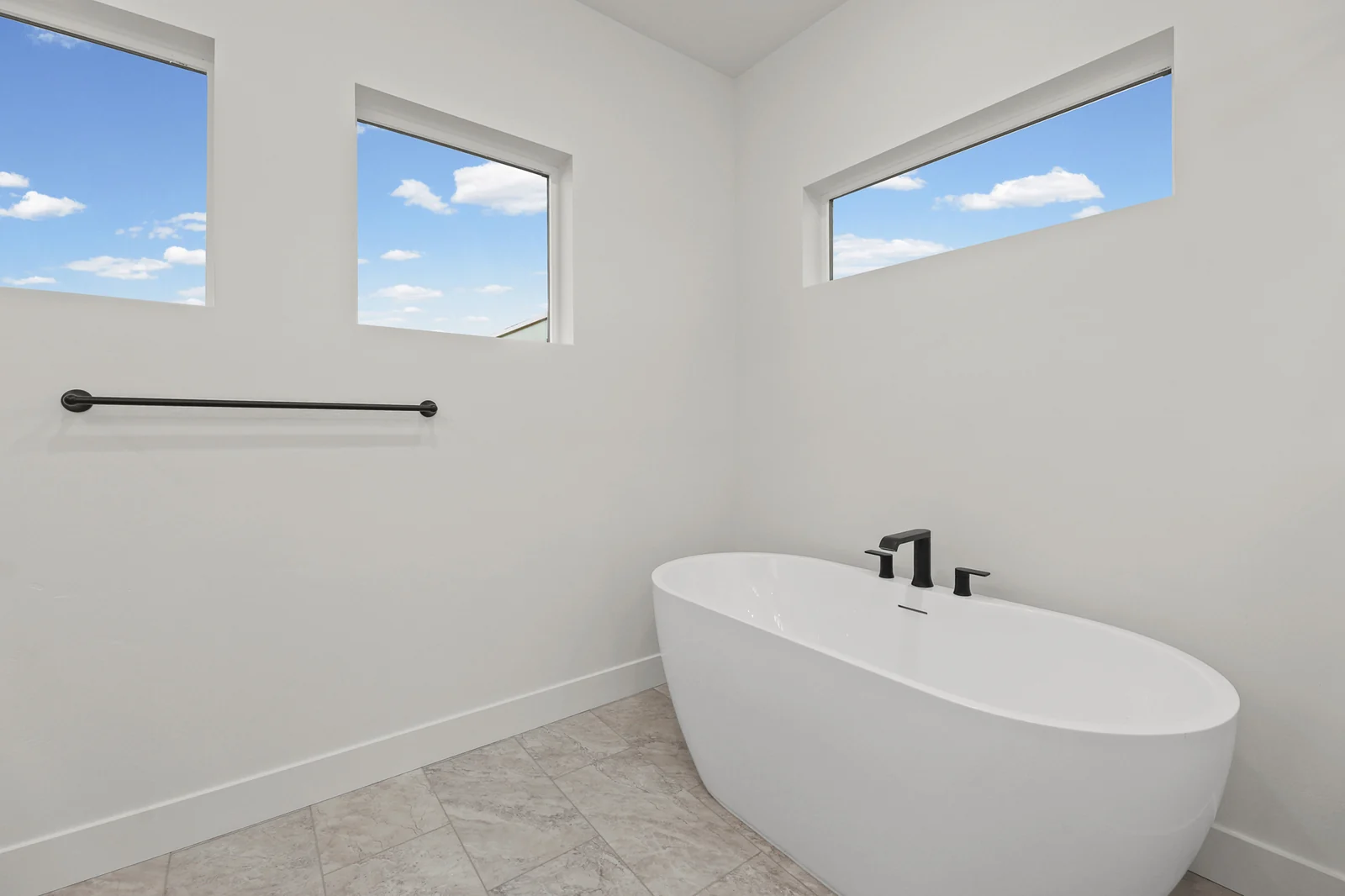 Bathroom with freestanding soaking tub, high windows, black fixtures, and light tile flooring in Hawthorne Modern, Ogden.