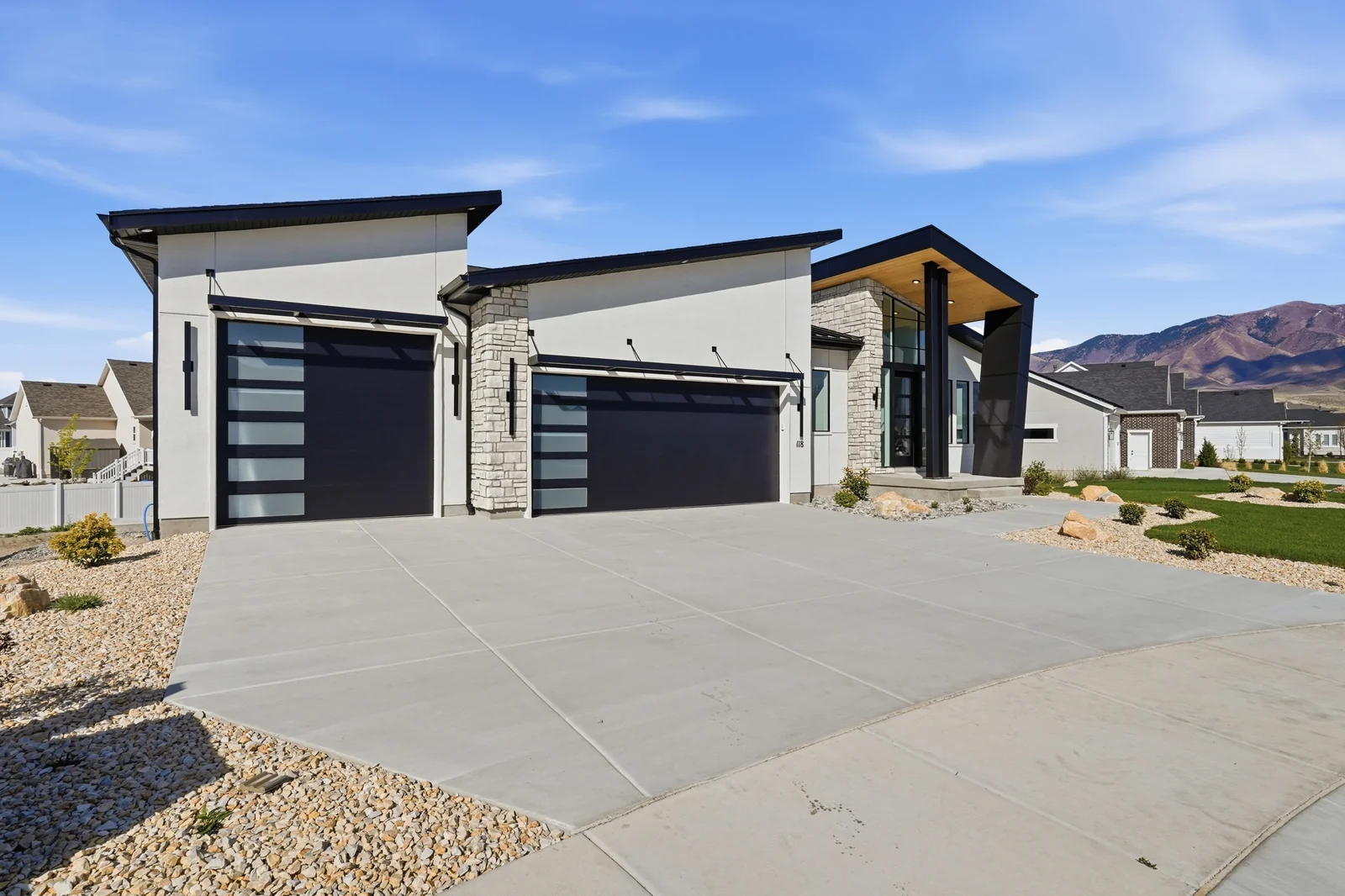 Daytime front exterior showing the concrete driveway, dark garage doors, stone accents, and landscaped beds in Chestnut Modern MW302, Stansbury Park.