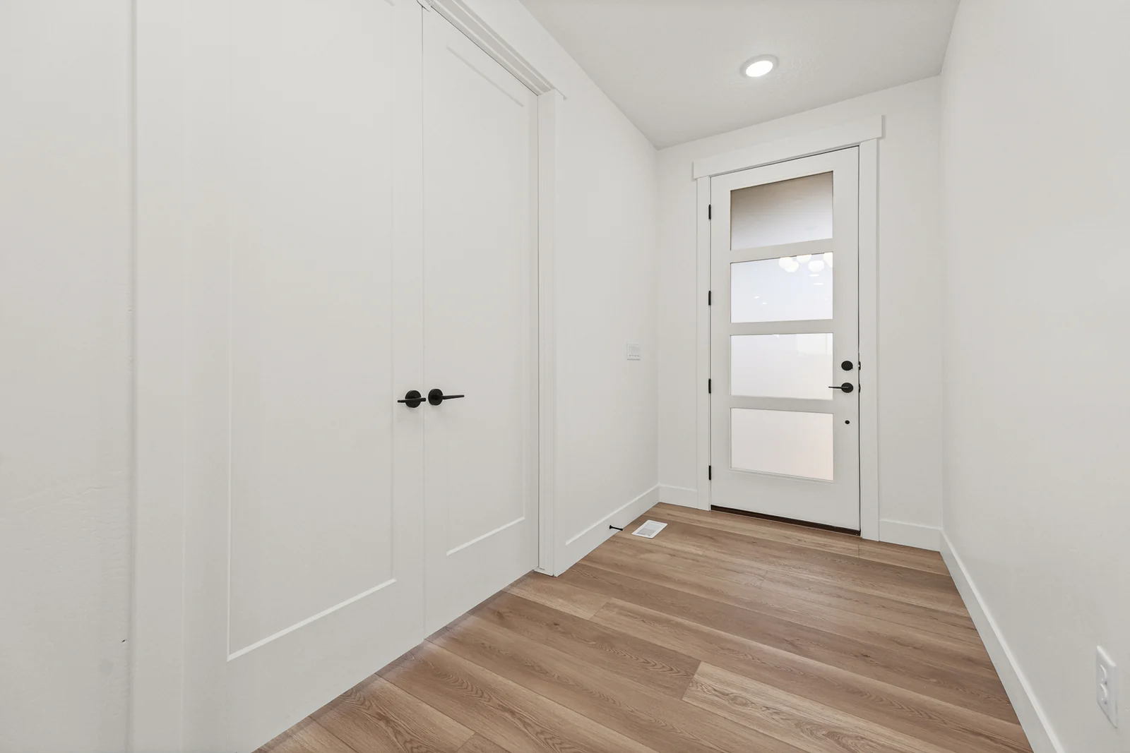 Interior hallway with wood-look flooring, white doors, recessed lights, and a glass-paneled exterior door in Hawthorne Modern, Ogden.