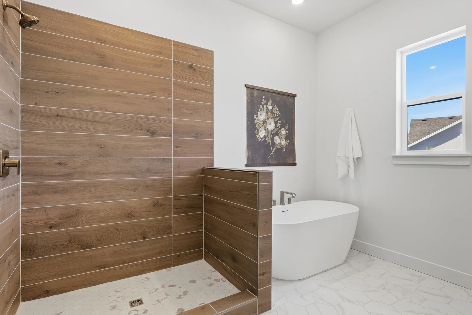 Bathroom corner with tiled shower, wood accent wall, freestanding tub, window, and white tile floor in Chestnut Modern MW302, Stansbury Park.