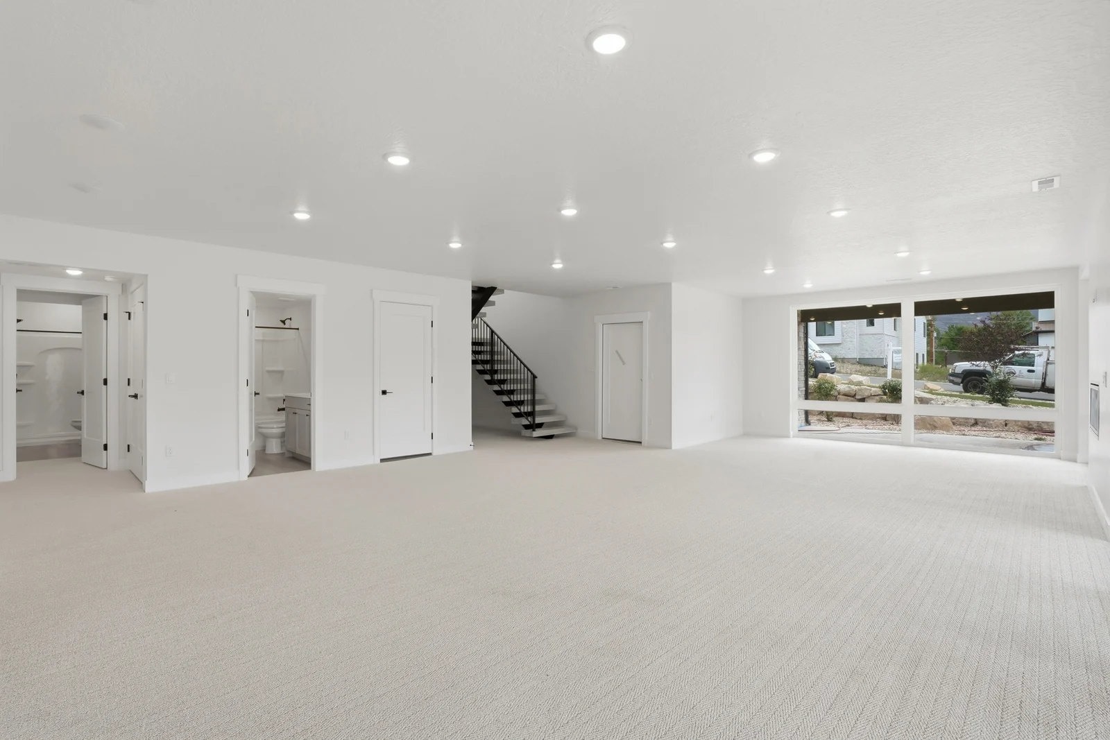 Wide view of the lower-level living area with pale carpet, staircase, fireplace wall, and sliding glass doors in the Denali model, American Fork.