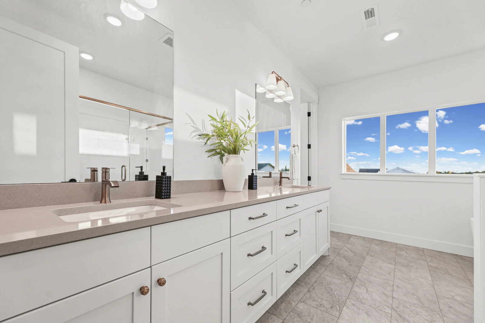 Bathroom double vanity has white cabinets, a long mirror, black fixtures, and tiled flooring in Hawthorne Farmhouse, Ogden.