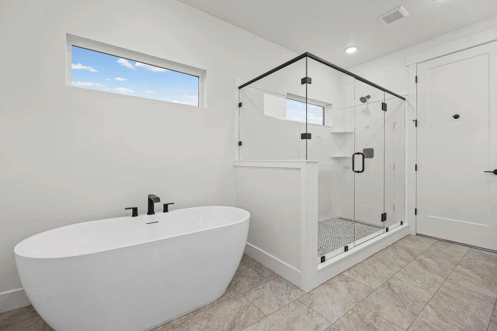 Primary bathroom with freestanding tub, glass shower enclosure, black fixtures, high window, and tile floor in Hawthorne Modern, Ogden.