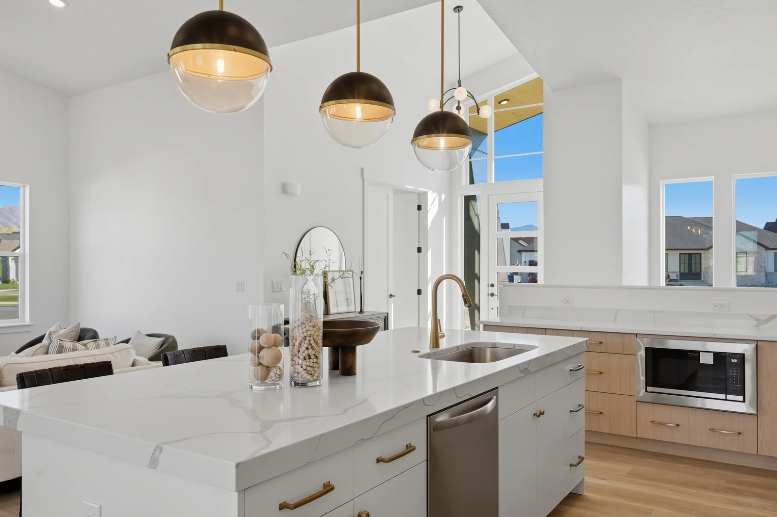 Kitchen island detail with sink, white countertop, pendant lights, dishwasher, and sightline into the living space in Chestnut Modern MW302, Stansbury Park.