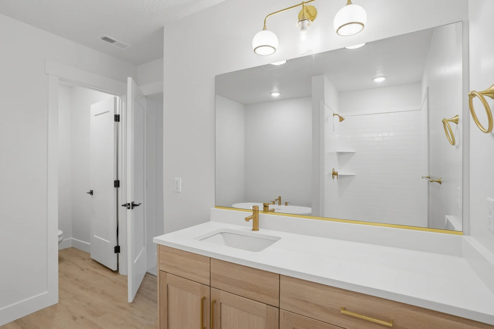 Bathroom with double vanity, large mirror, gold-toned fixtures, shower enclosure, and white walls in Olympic BH08, American Fork.