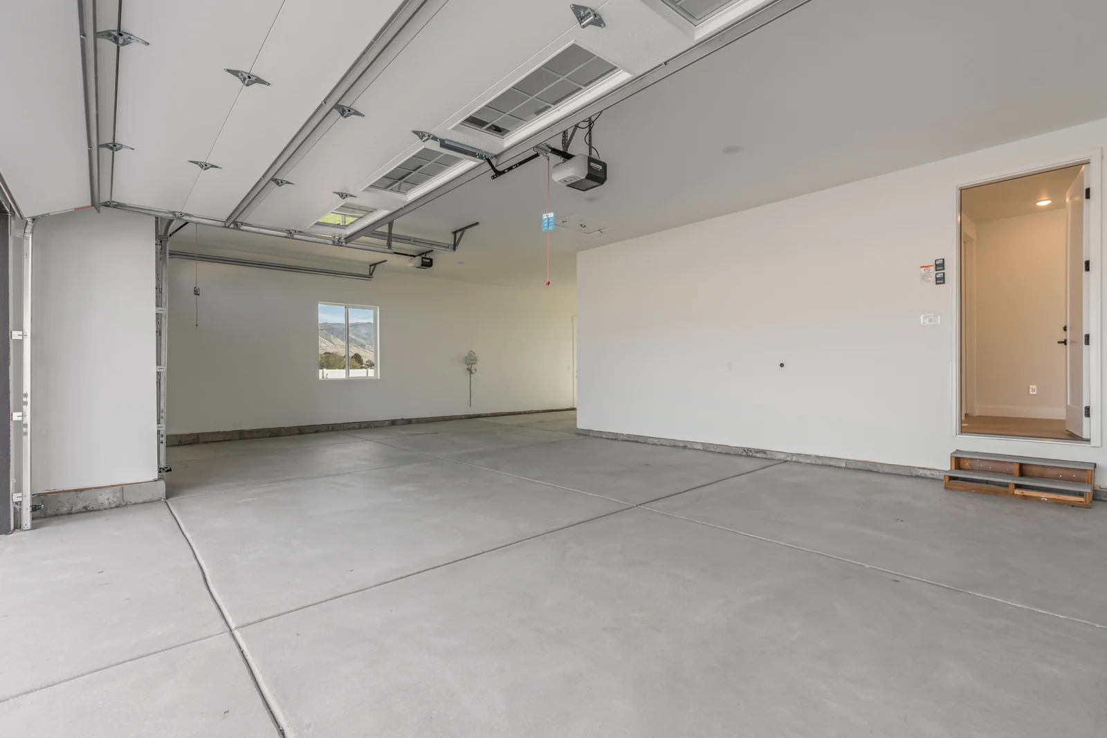 Wide attached garage with concrete floor, overhead door tracks, exterior access door, and wall cabinets at Chestnut MW311, Stansbury Park.
