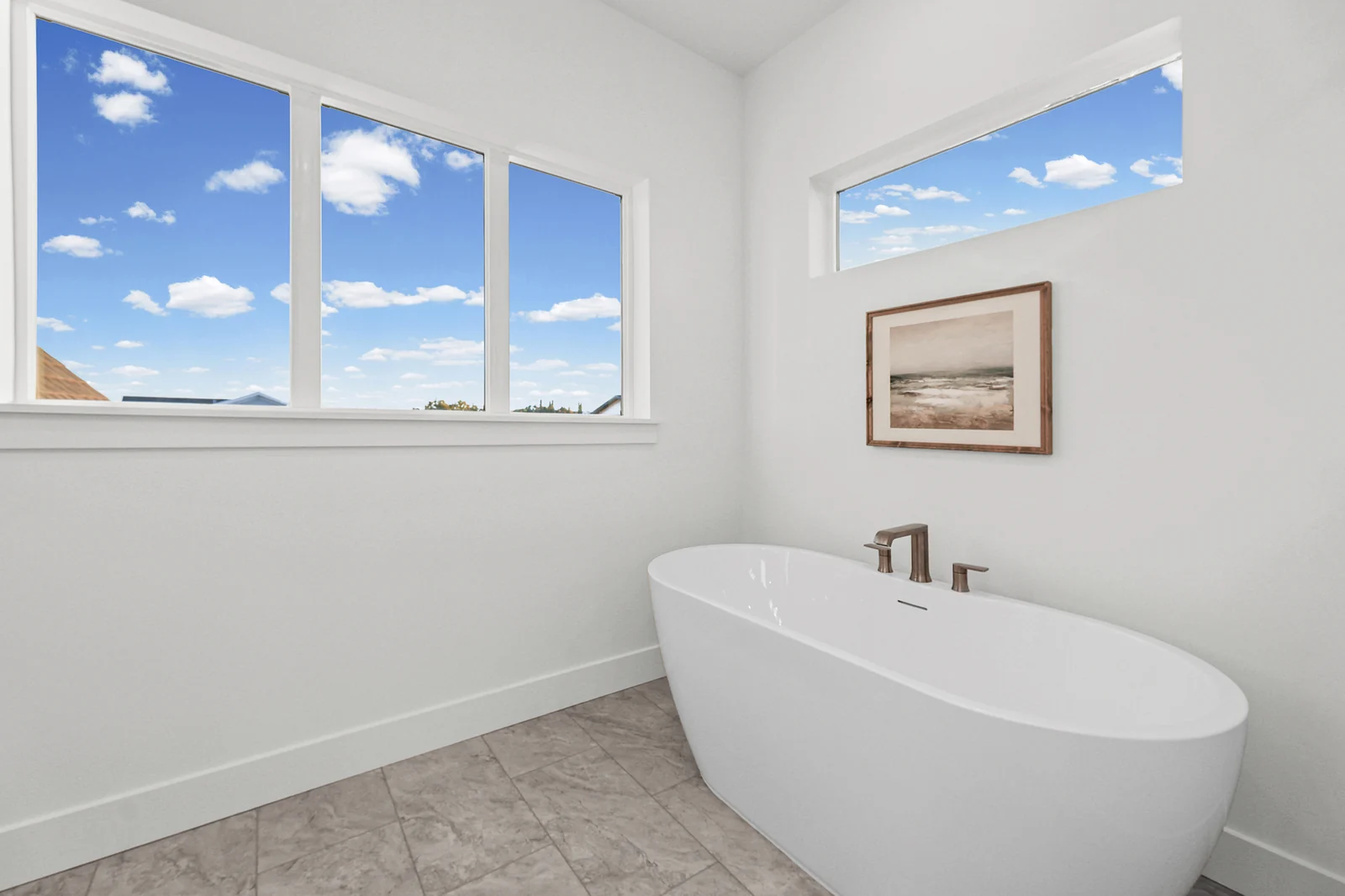 Freestanding tub rests beneath large windows in a bright tiled bathroom with a framed picture in Hawthorne Farmhouse, Ogden.