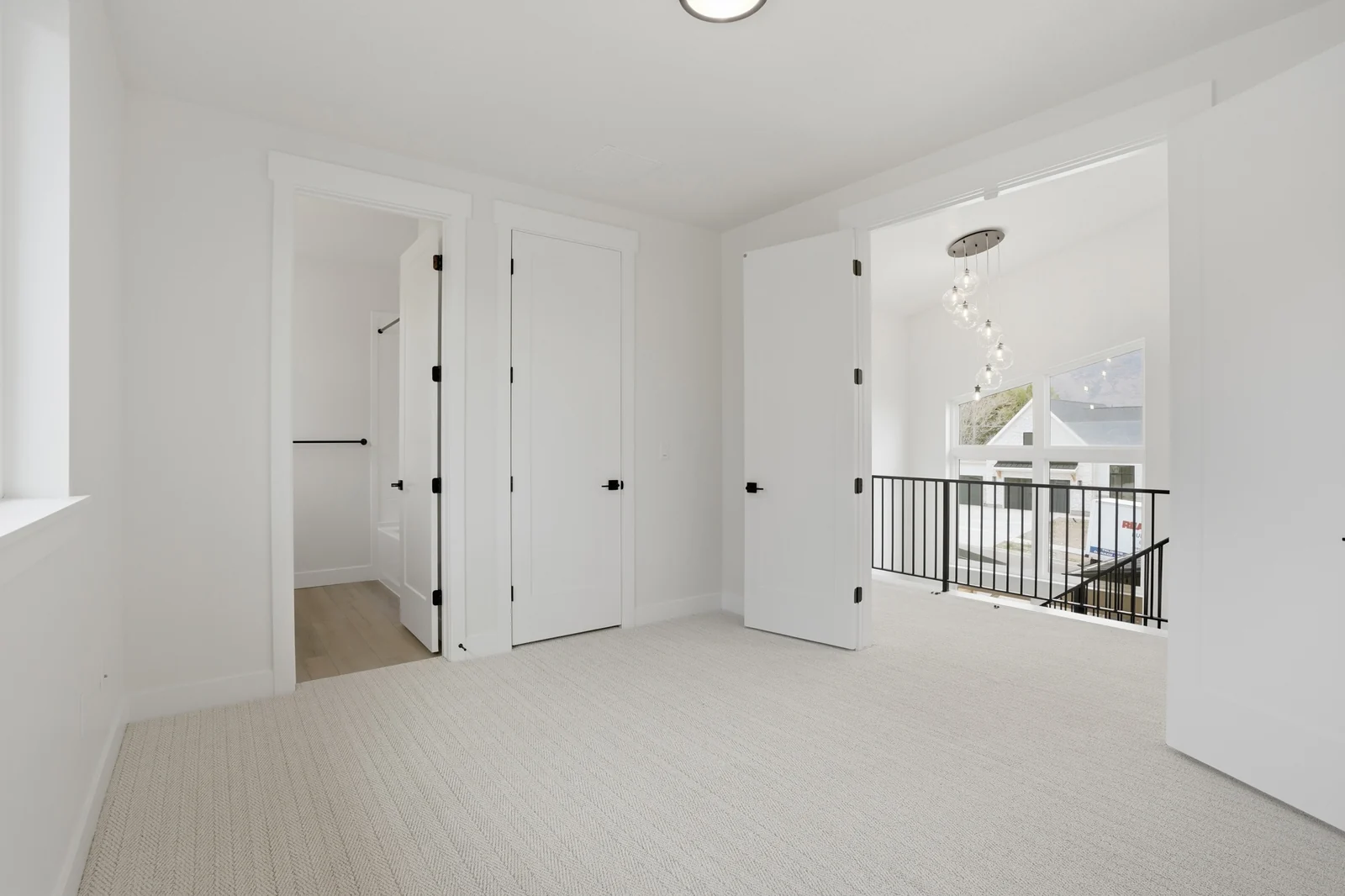 Upper hall with pale carpeting, white doors, a window, and an open stair railing visible at the far end in the Denali model, American Fork.