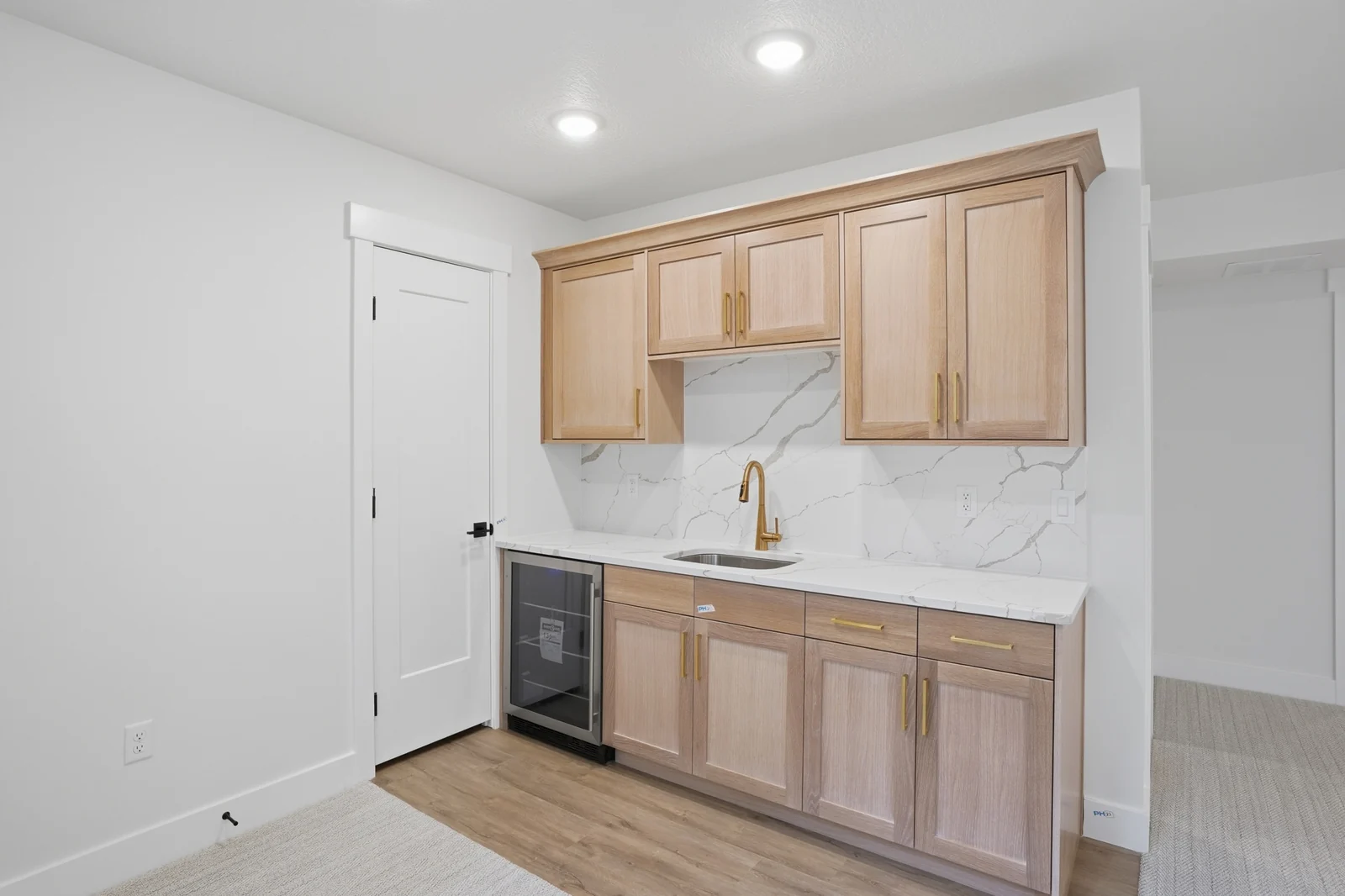 Lower-level beverage bar with wood cabinetry, small sink, undercounter appliance, and white walls in Olympic BH08, American Fork.