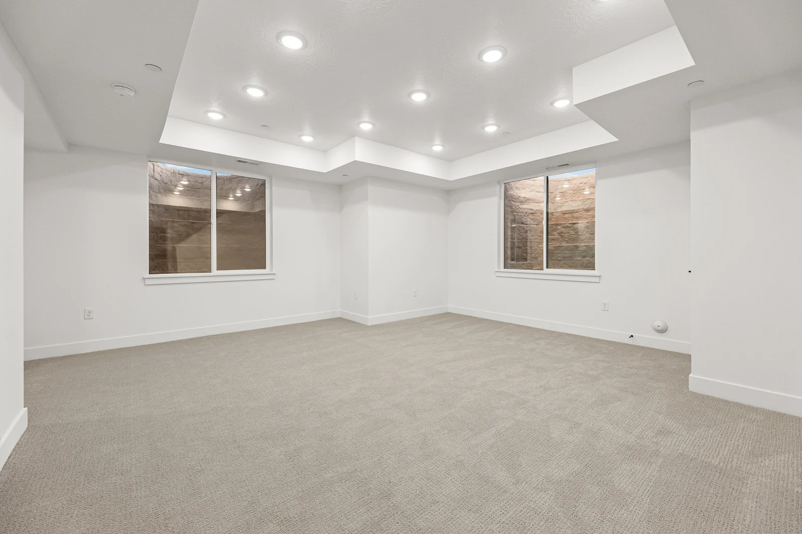 Carpeted lower-level recreation room with tray ceiling, recessed lights, windows, and white support columns in Hawthorne Modern, Ogden.