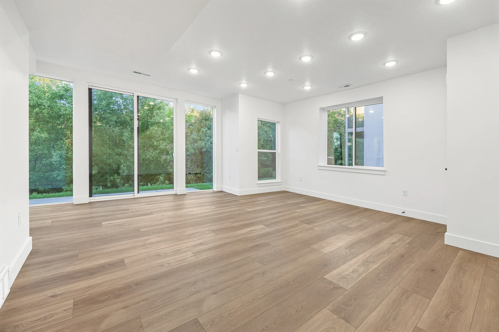Unfurnished lower-level room has wood flooring, multiple windows, recessed lights, and sliding glass doors in Hawthorne Farmhouse, Ogden.