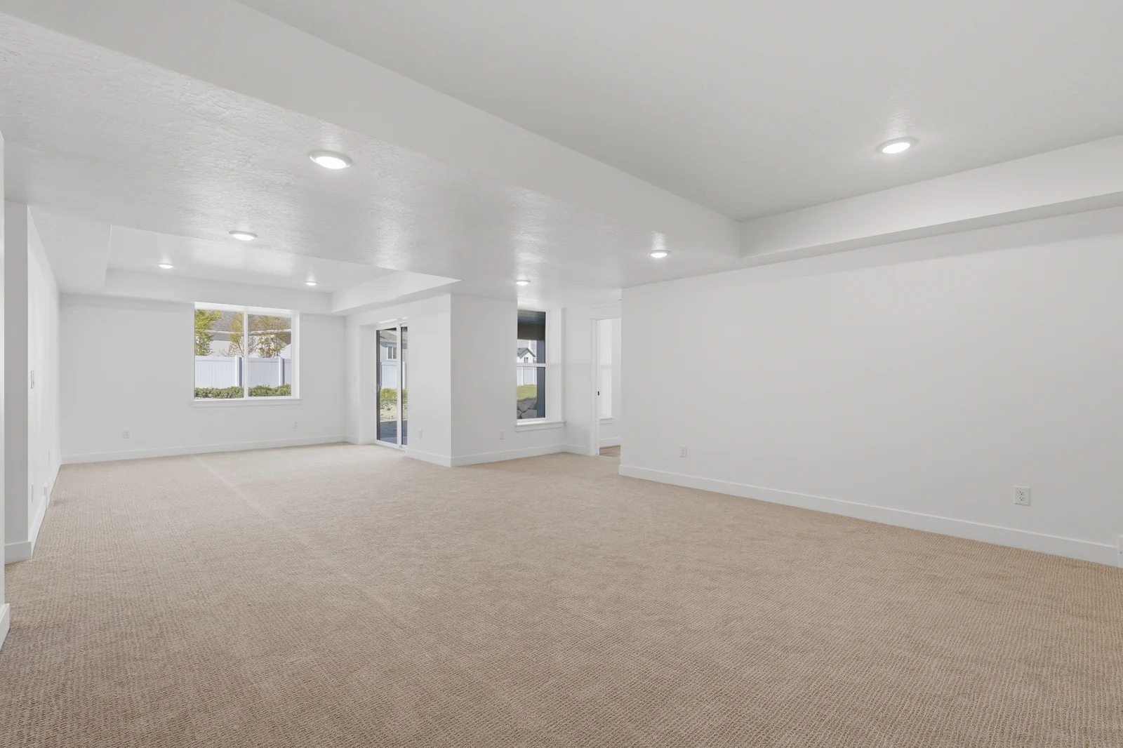 Second view of an open carpeted room with recessed lights, windows, white walls, and columns in Chestnut Modern MW302, Stansbury Park.