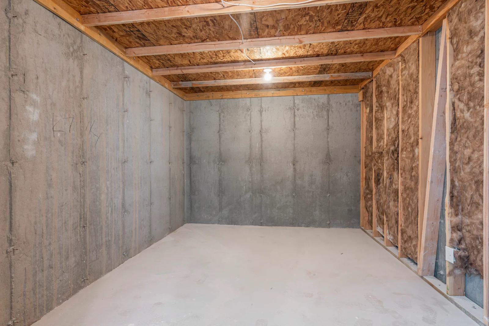 Unfinished lower-level space with exposed stud walls, insulation, concrete foundation, ceiling framing, and open doorway at Chestnut MW311, Stansbury Park.