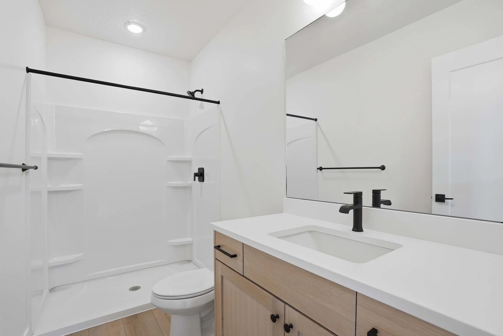 Bathroom with a wood vanity, white countertop, toilet, and molded tub-shower combination under a dark shower rod in the Denali model, American Fork.