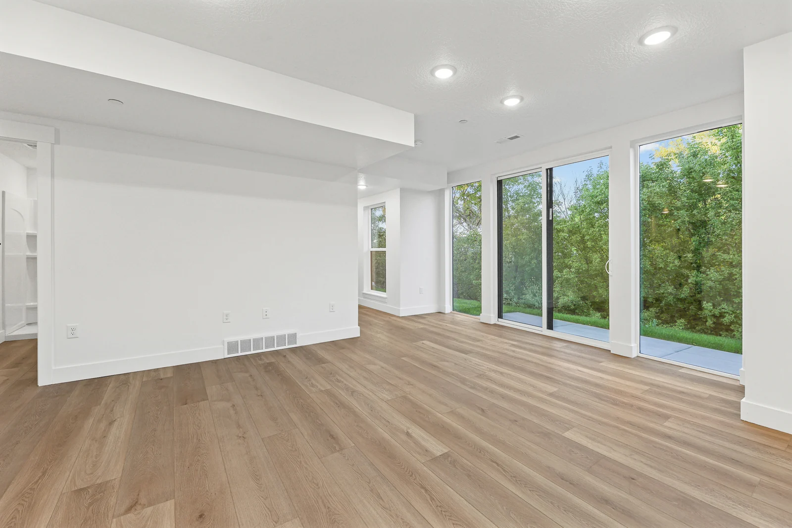 Unfurnished lower-level room features a broad open floor, tall windows, sliding doors, and white walls in Hawthorne Farmhouse, Ogden.