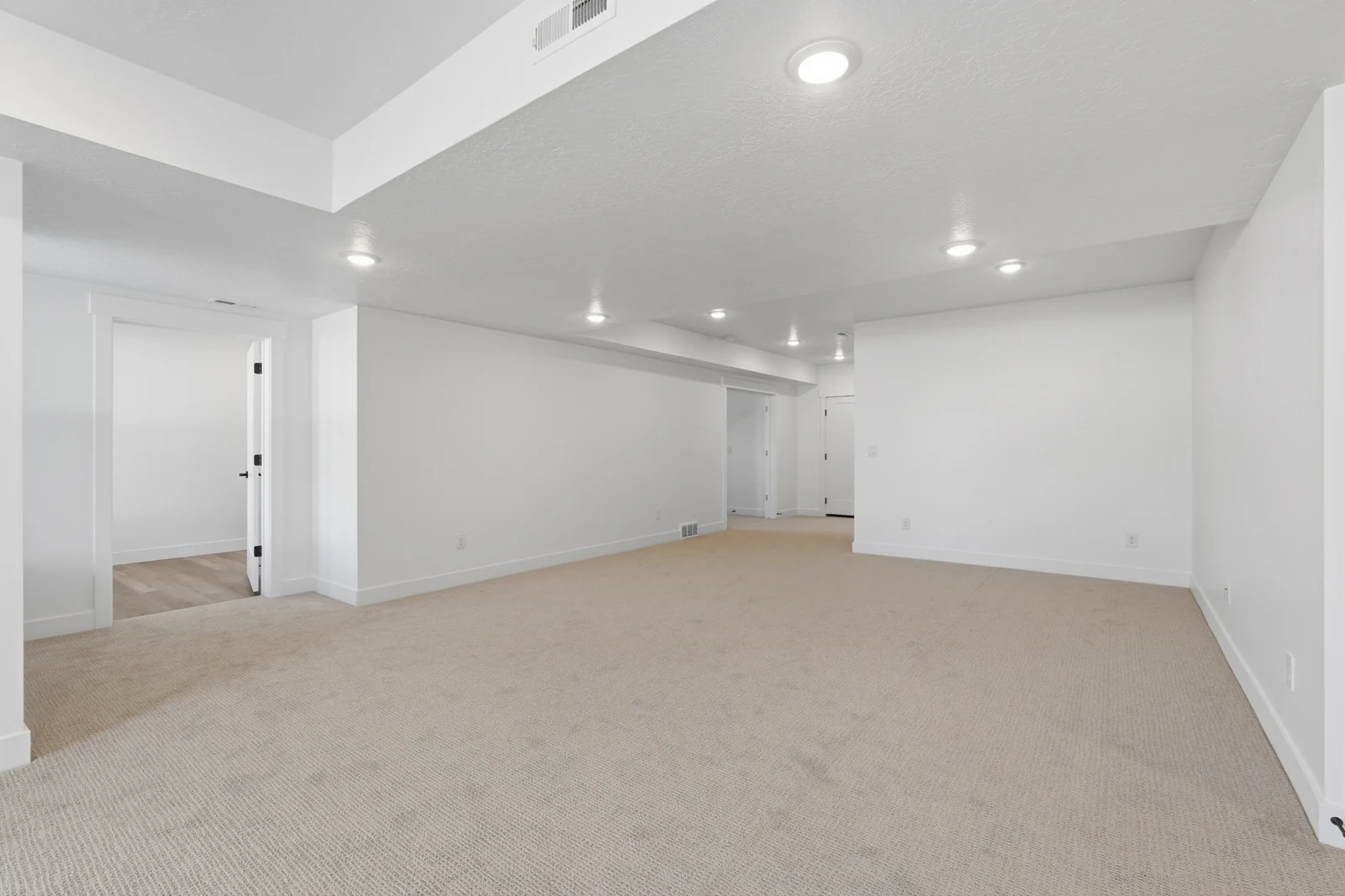Wide view of a carpeted open room with a tray ceiling, recessed lighting, columns, and doorways in Chestnut Modern MW302, Stansbury Park.