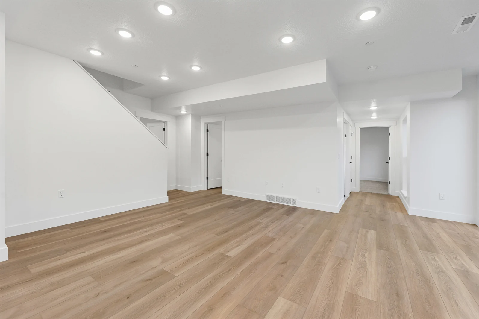 Open lower-level room has wood flooring, recessed lighting, a stairway, and several interior doors in Hawthorne Farmhouse, Ogden.