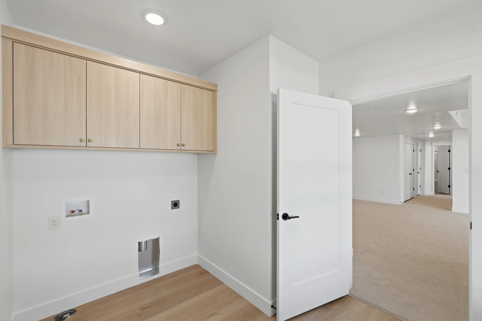 Laundry room with upper wood cabinets, washer and dryer hookups, light flooring, and an open door in Chestnut Modern MW302, Stansbury Park.