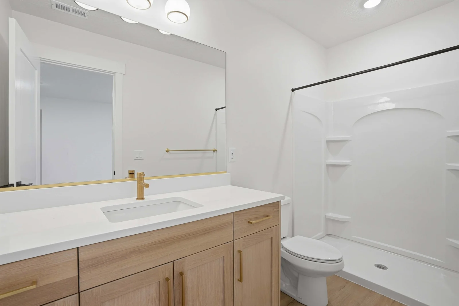Bathroom with wood vanity, large mirror, tub-shower combination, and gold-toned fixtures in Olympic BH08, American Fork.