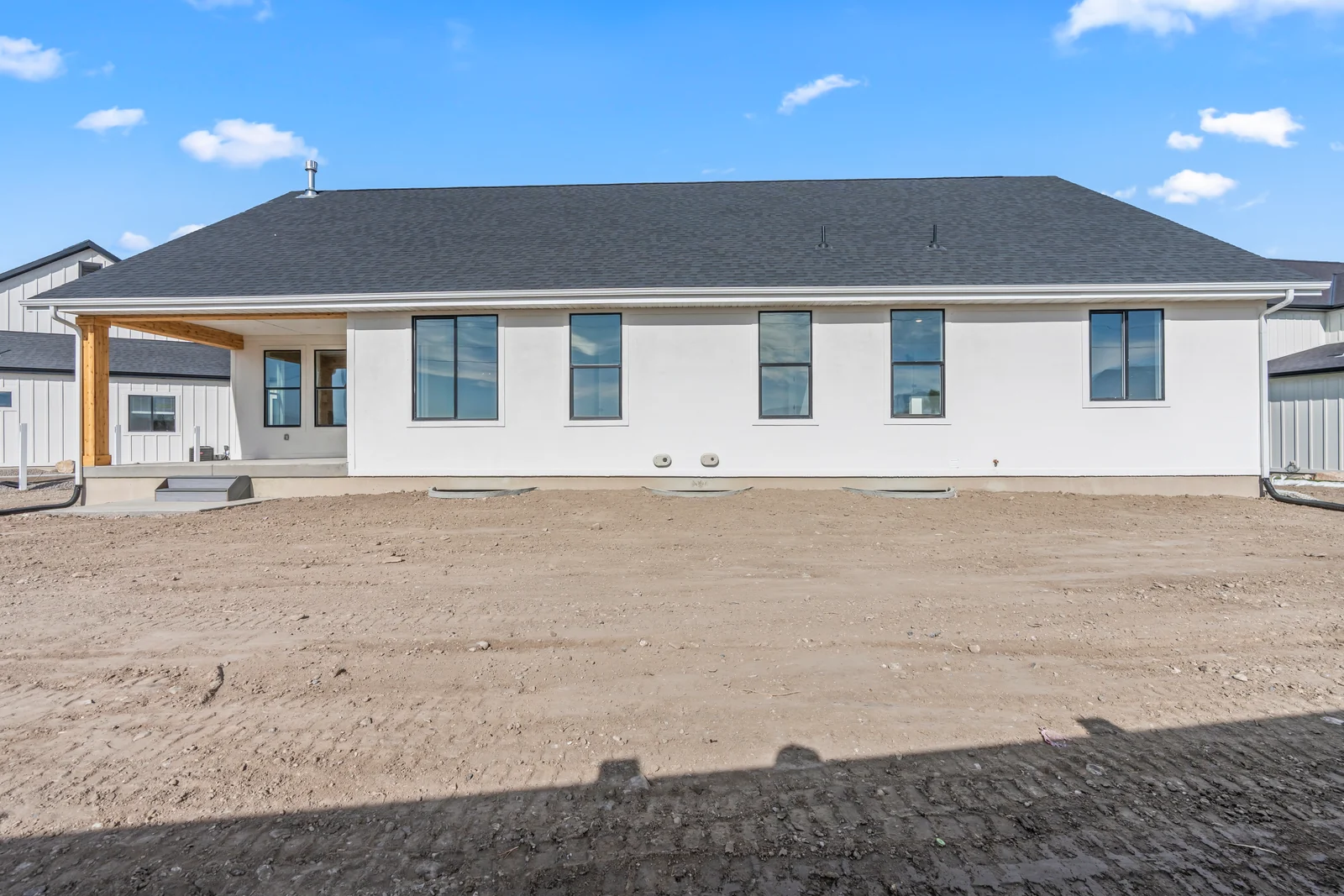 Wide rear view of the home showing covered patio, windows, siding, and surrounding unlandscaped ground at Chestnut MW311, Stansbury Park.