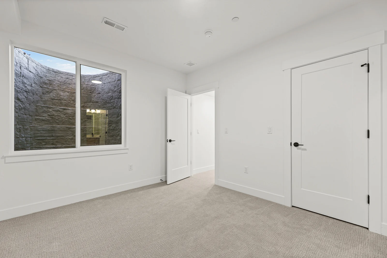Unfurnished carpeted lower-level bedroom with window, double closet doors, interior doorway, and white trim in Hawthorne Modern, Ogden.