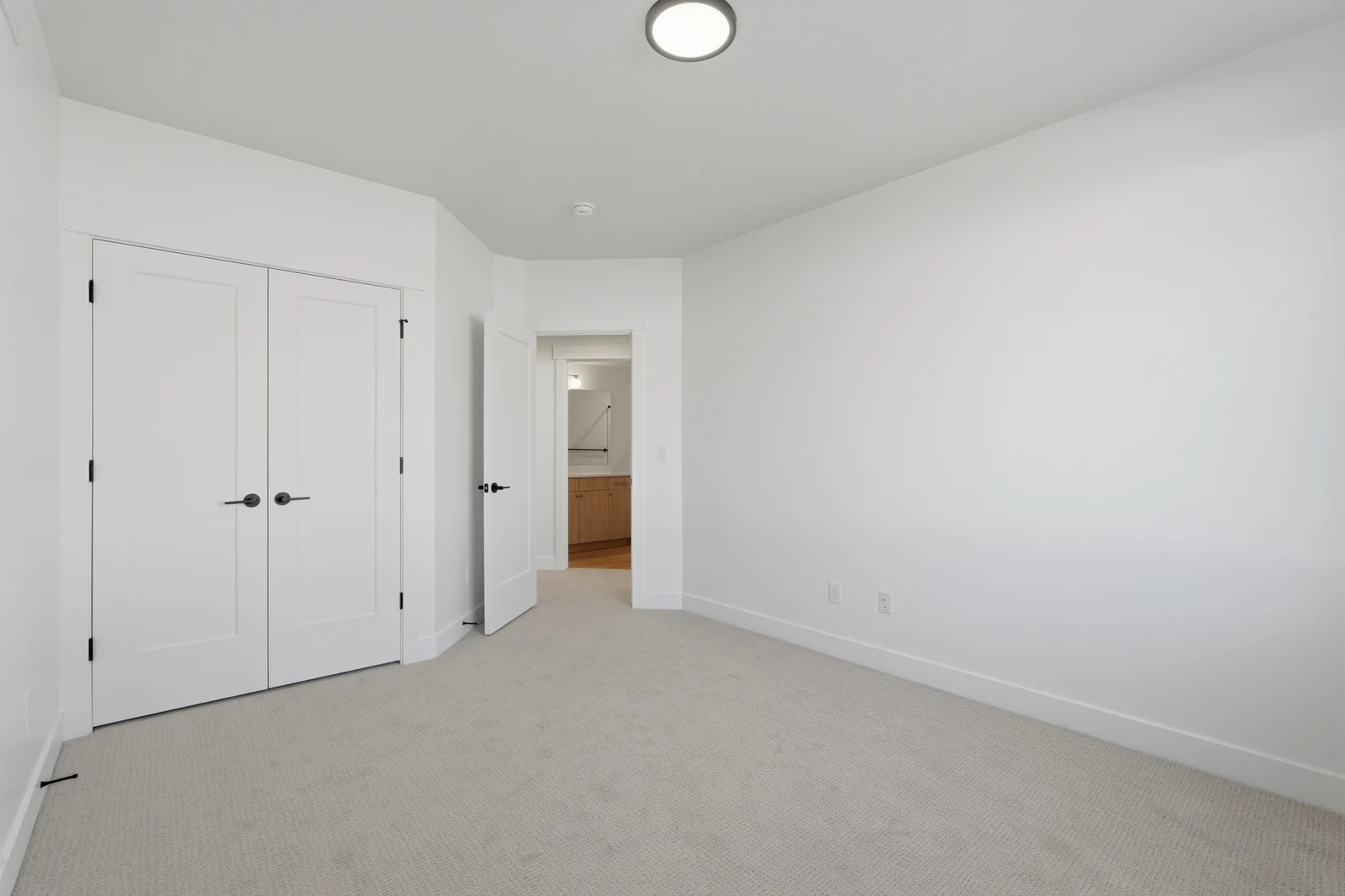 Empty carpeted bedroom with a double-door closet, white walls, recessed lighting, and hallway entry in Chestnut Modern MW302, Stansbury Park.