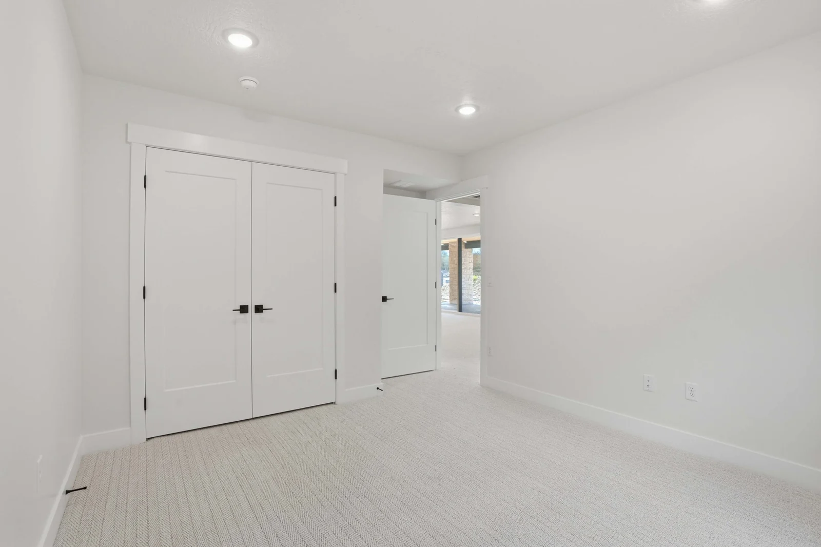 Unfurnished bedroom view showing pale carpet, white double closet doors, recessed lights, and the adjoining hallway in the Denali model, American Fork.