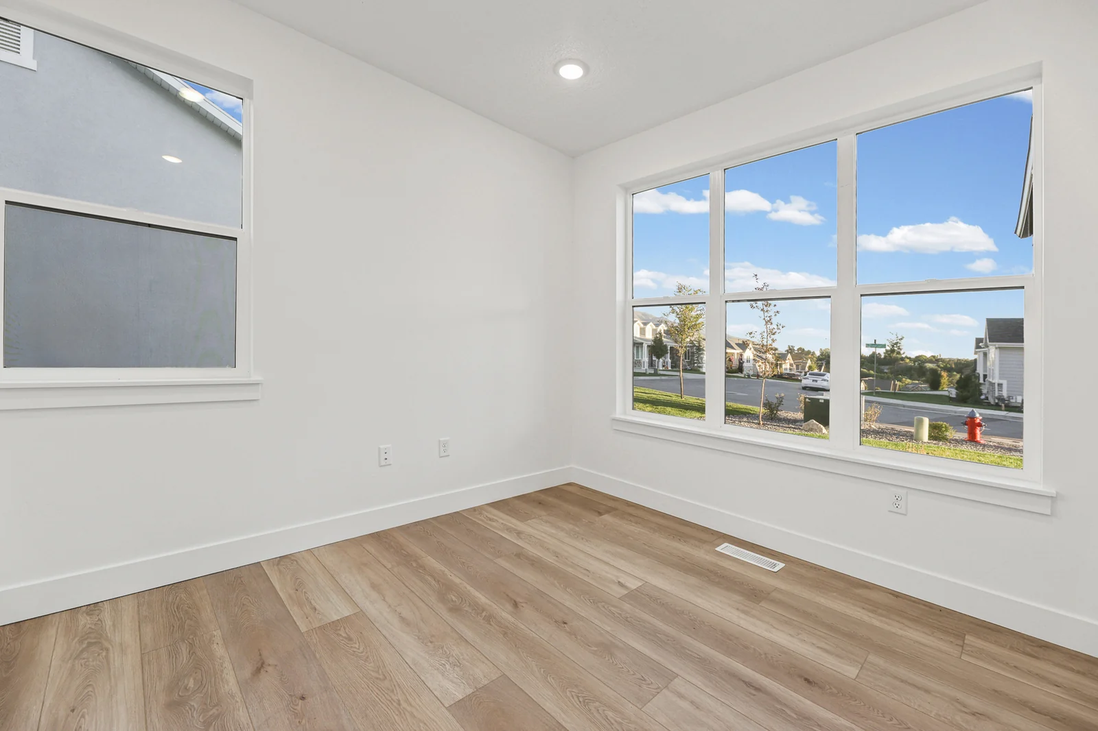 Unfurnished room features light wood flooring, tall windows, white walls, and roller shades in Hawthorne Farmhouse, Ogden.