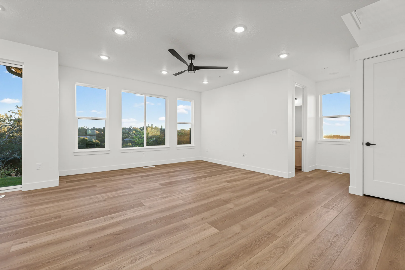 Open great room with wood-look flooring, ceiling fan, recessed lights, large windows, and stairway in Hawthorne Modern, Ogden.