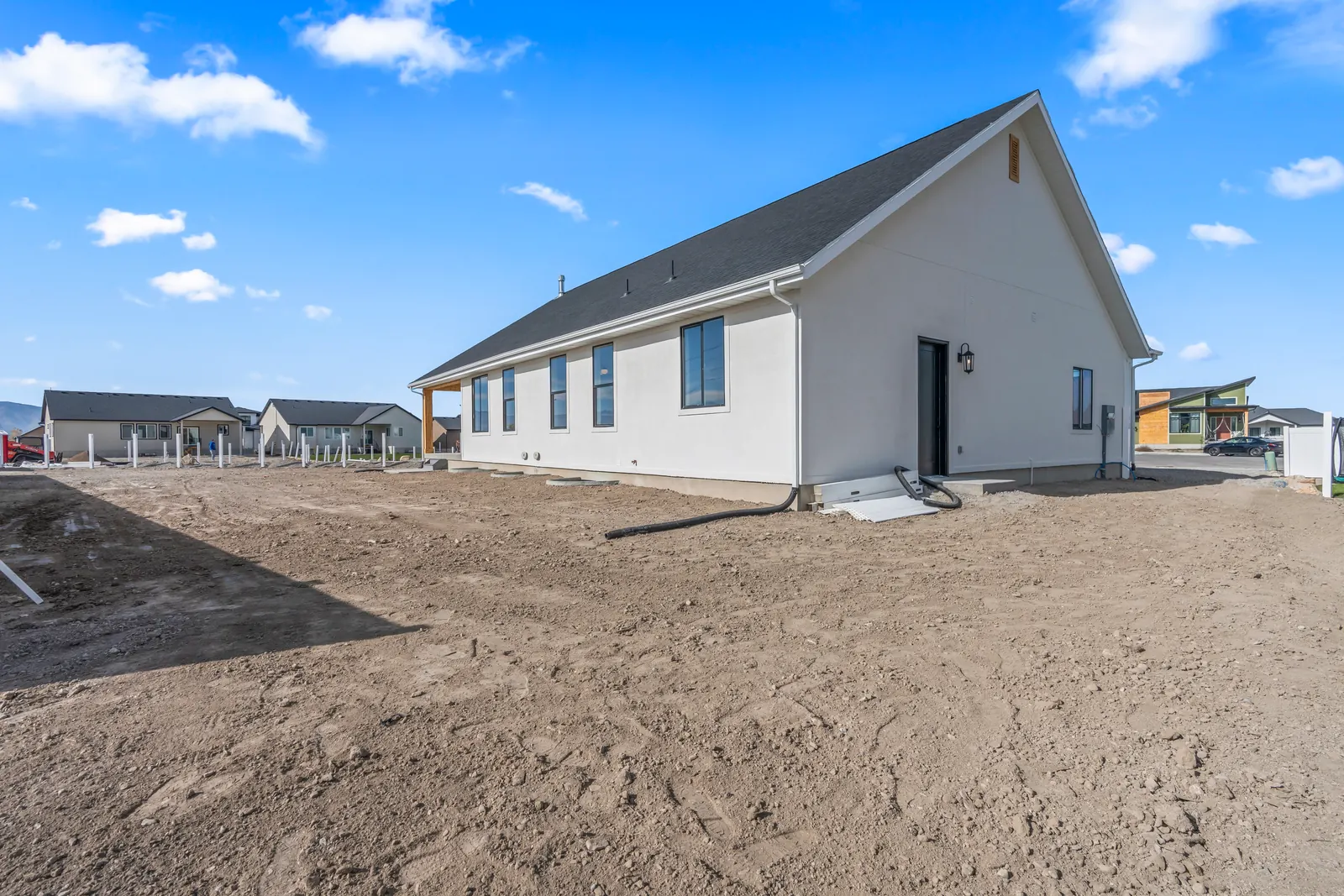 Side exterior view with white siding, several windows, roofline, and unlandscaped ground beside the home at Chestnut MW311, Stansbury Park.