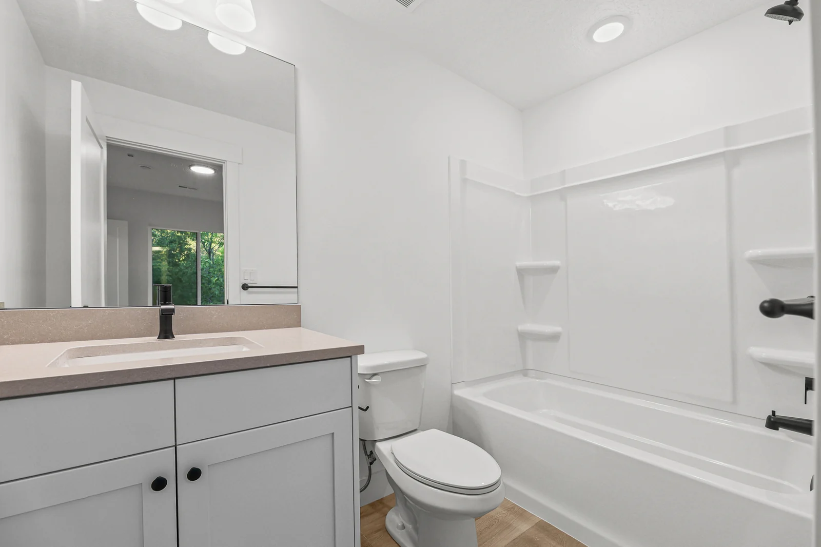 Bathroom vanity with black faucet faces a white tub-shower, toilet, and built-in shelving in Hawthorne Farmhouse, Ogden.
