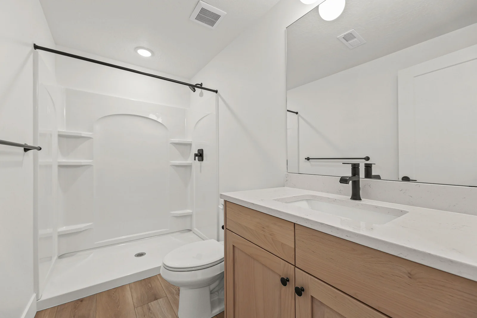 Lower-level bathroom with wood vanity, white countertop, black faucet, tub-shower surround, and toilet in Hawthorne Modern, Ogden.