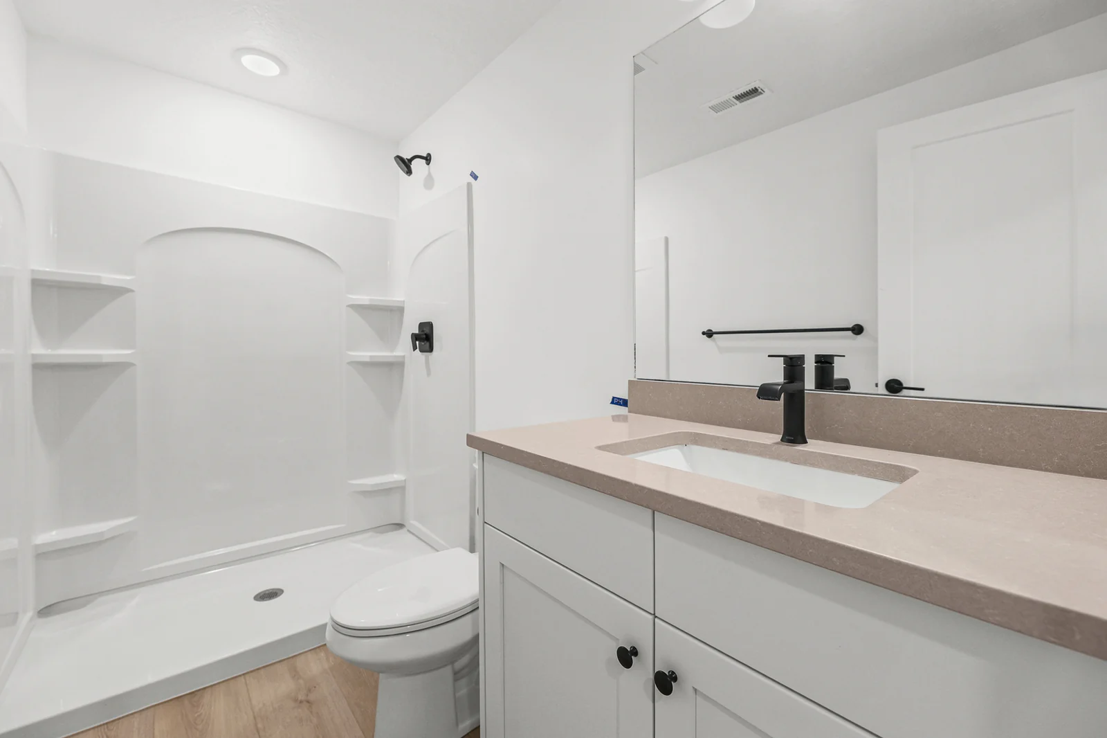 White tub-shower combination includes inset shelves, a toilet, and vanity countertop in Hawthorne Farmhouse, Ogden.