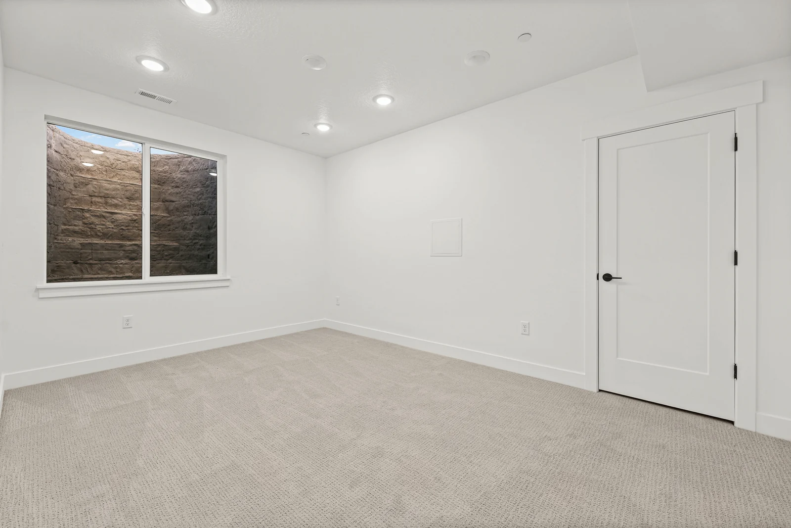 Unfurnished carpeted lower-level bedroom with window, white closet doors, recessed lights, and an interior door in Hawthorne Modern, Ogden.