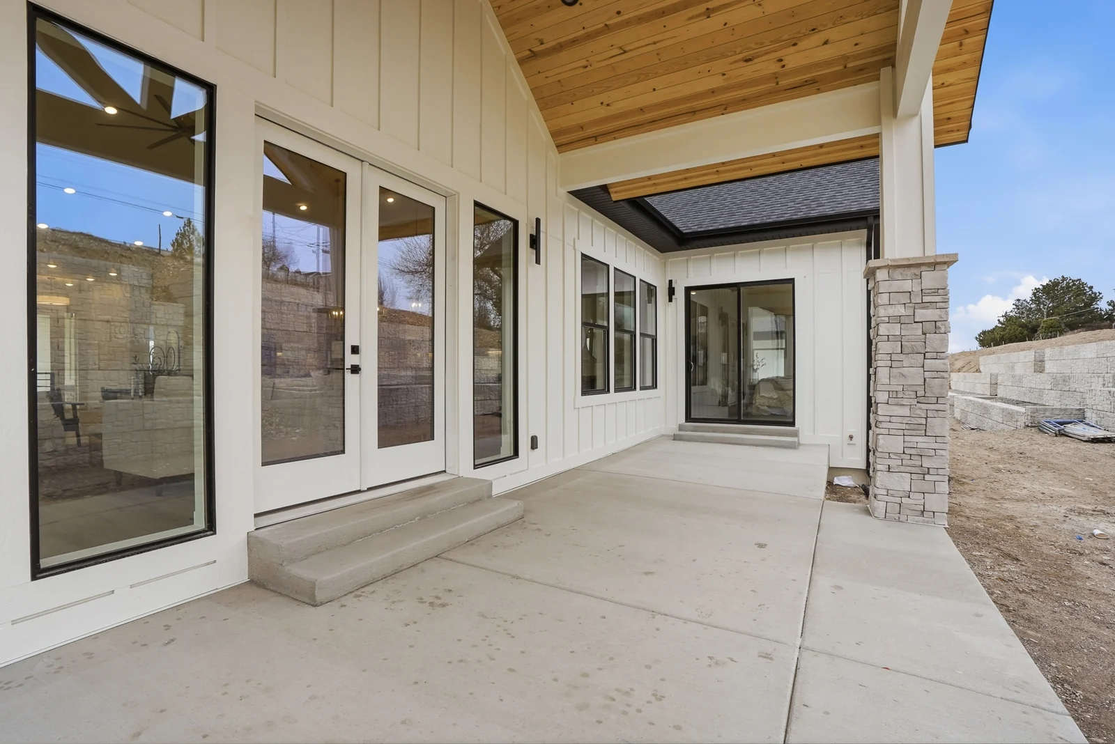 Covered rear patio with black-framed doors, stone columns, timber ceiling, and concrete floor in Olympic BH08, American Fork.