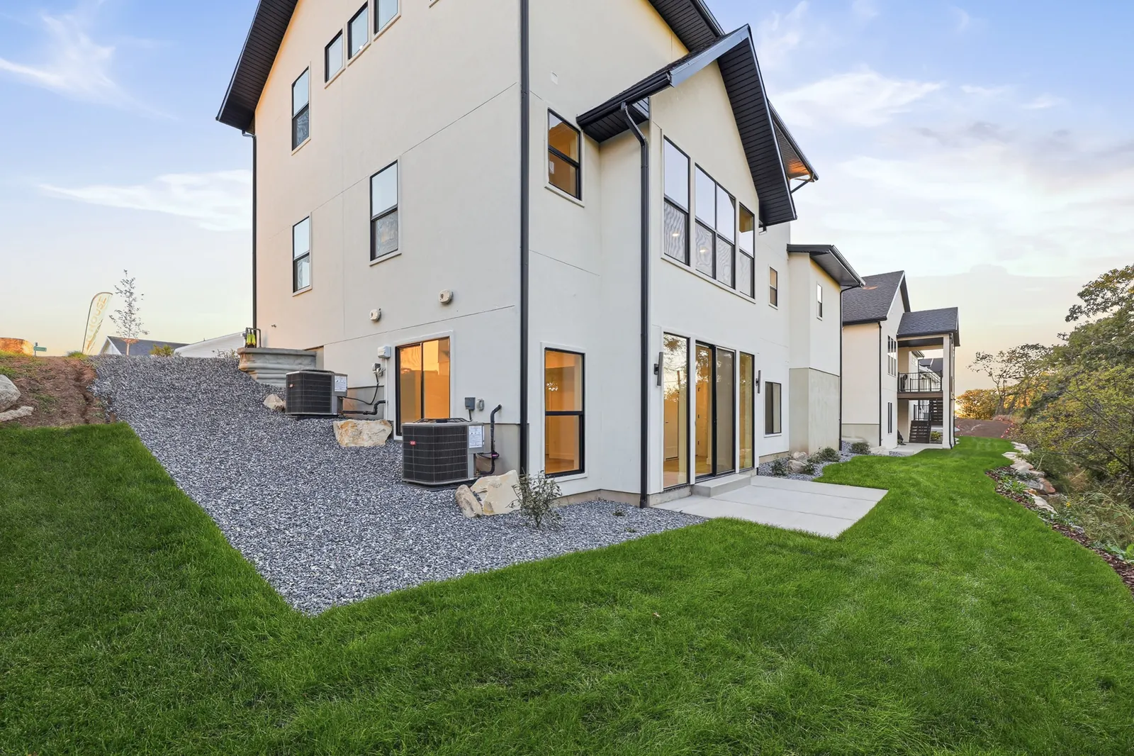 Concrete rear patio opens to a narrow lawn beside trees, shrubs, and the home exterior in Hawthorne Farmhouse, Ogden.