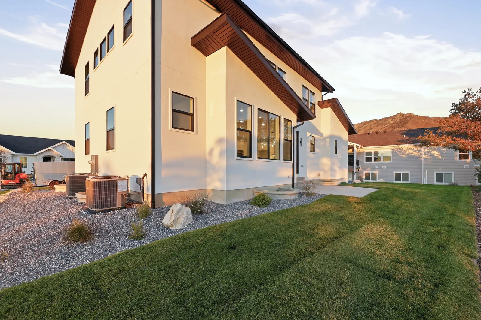 Rear exterior with white siding, dark roofline, lawn, gravel border, and neighboring homes at dusk in Hawthorne Modern, Ogden.
