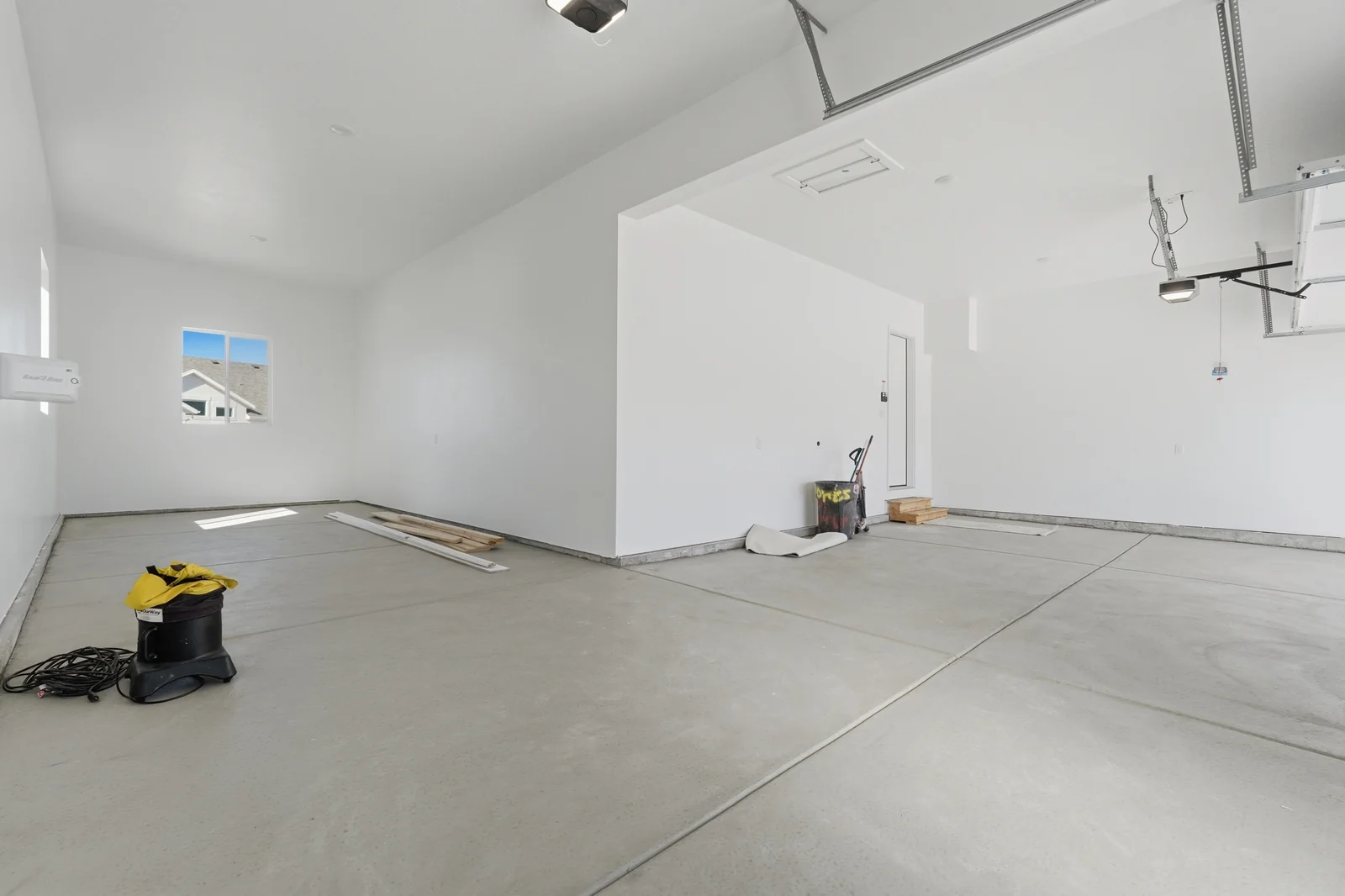 Garage interior with two overhead door tracks, concrete floor, window, and visible construction materials in Chestnut Modern MW302, Stansbury Park.