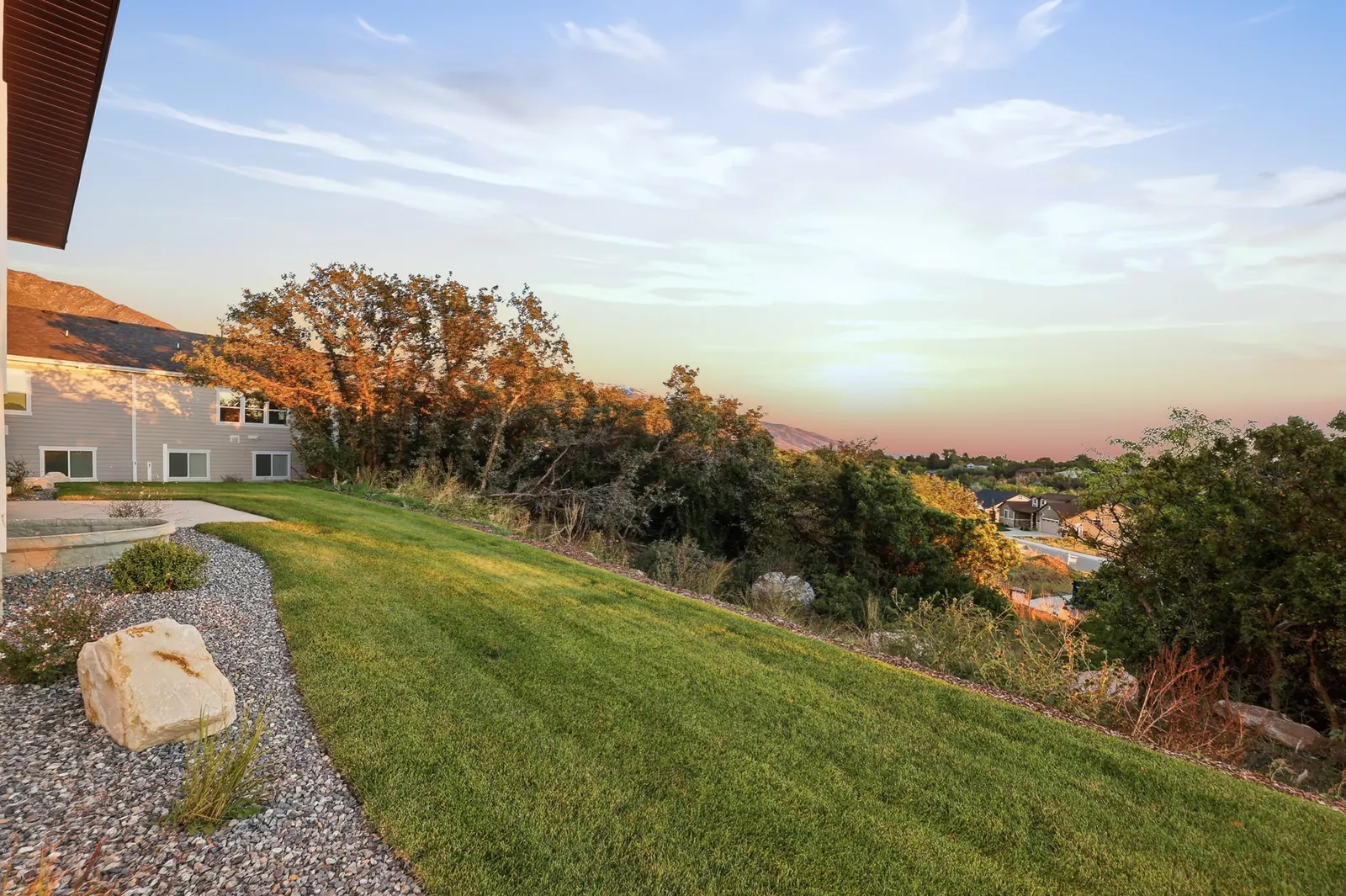 Side and rear exterior with large windows, lawn, gravel landscaping, and nearby homes at dusk in Hawthorne Modern, Ogden.