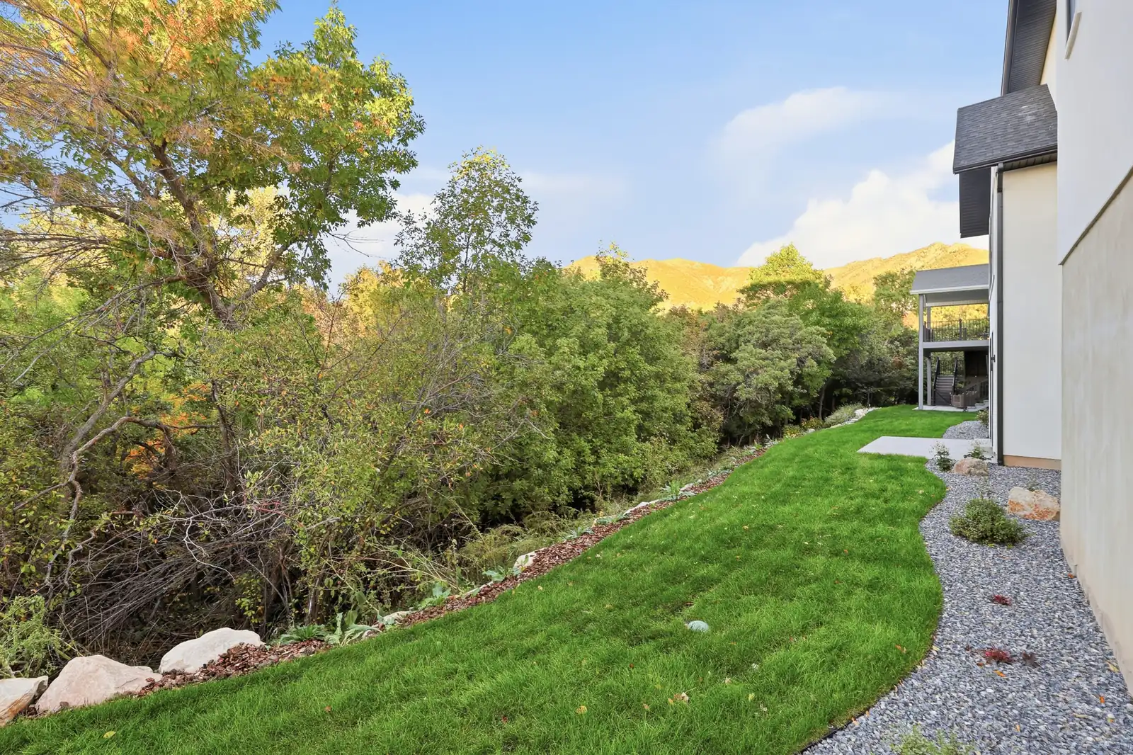Side lawn runs beside gravel landscaping, trees, shrubs, and the rear portion of the home in Hawthorne Farmhouse, Ogden.