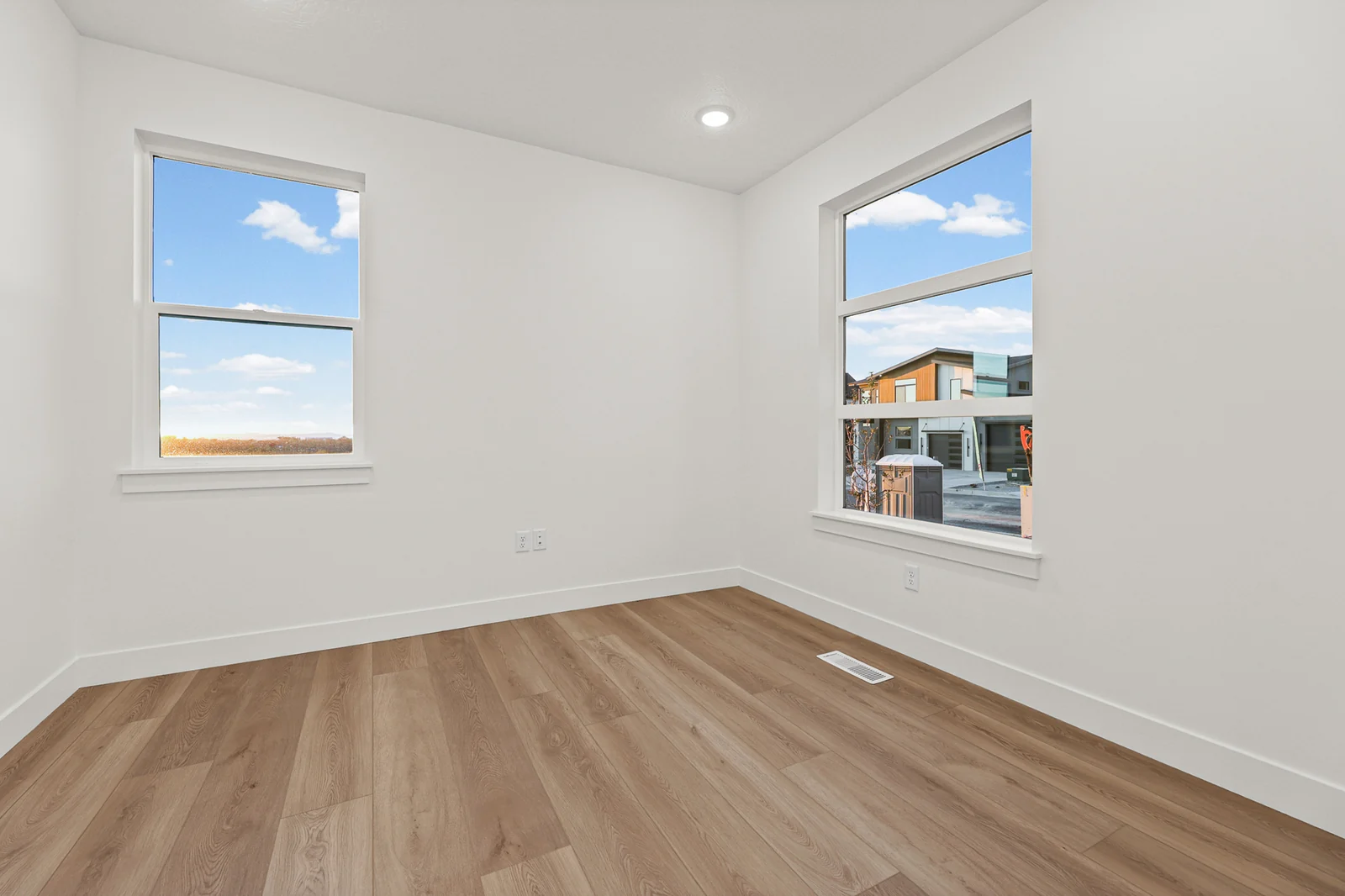Unfurnished bedroom with wood-look flooring, two corner windows, white walls, and a nearby neighboring home in Hawthorne Modern, Ogden.