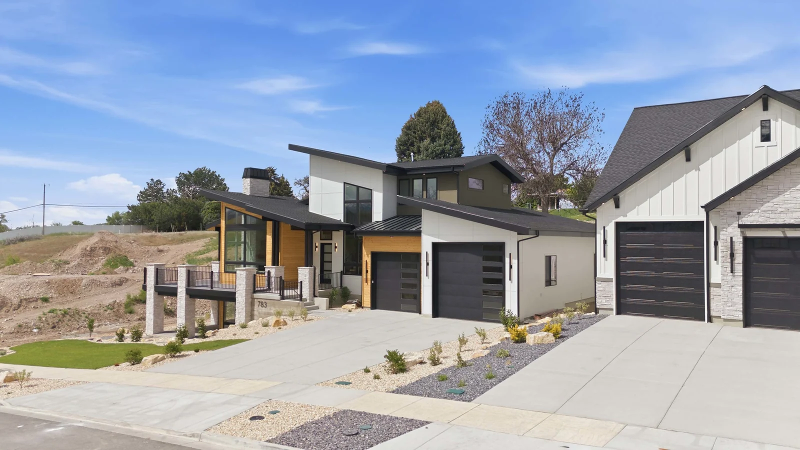 Oblique aerial view of the front facade, concrete driveway, landscaped beds, adjacent homes, and distant foothills in the Denali model, American Fork.