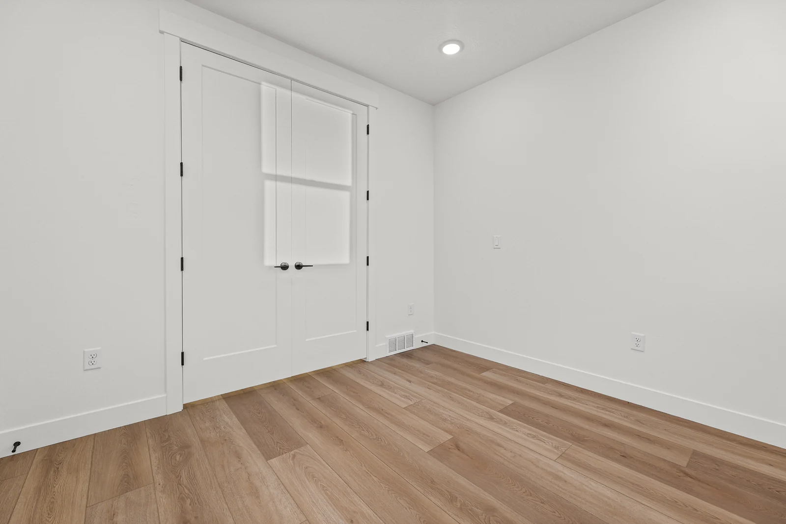 Unfurnished bedroom with wood-look flooring, double closet doors, white walls, and an interior door in Hawthorne Modern, Ogden.