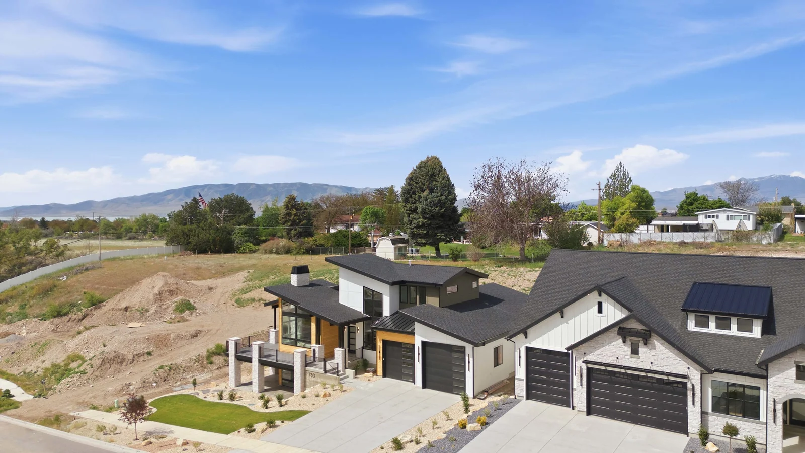 Elevated aerial view showing the roofline, driveway, garage doors, neighboring roofs, and the surrounding residential setting in the Denali model, American Fork.
